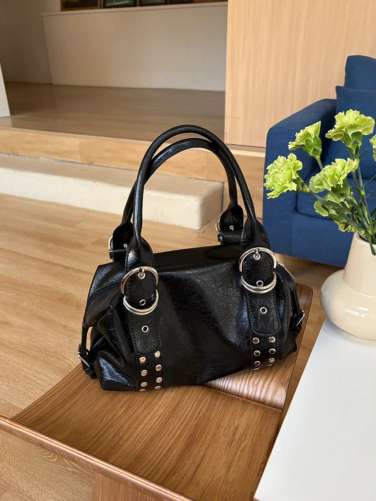A black soft PU leather shoulder bag with silver rivet accents resting on a wooden surface.