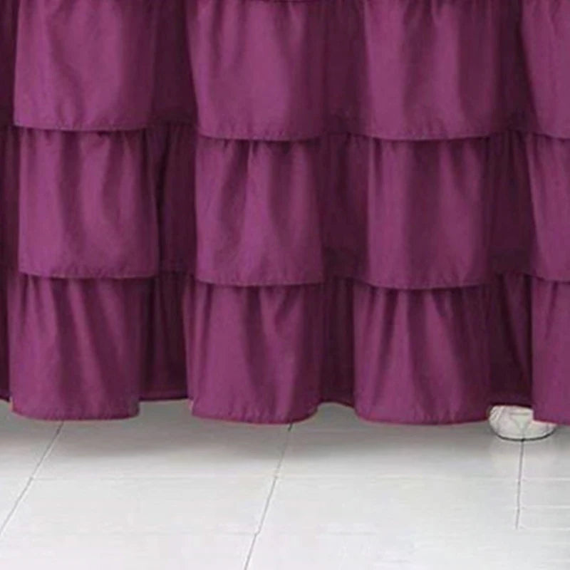 A deep purple ruffled bed skirt made of elastic fabric covering the bottom of a mattress.
