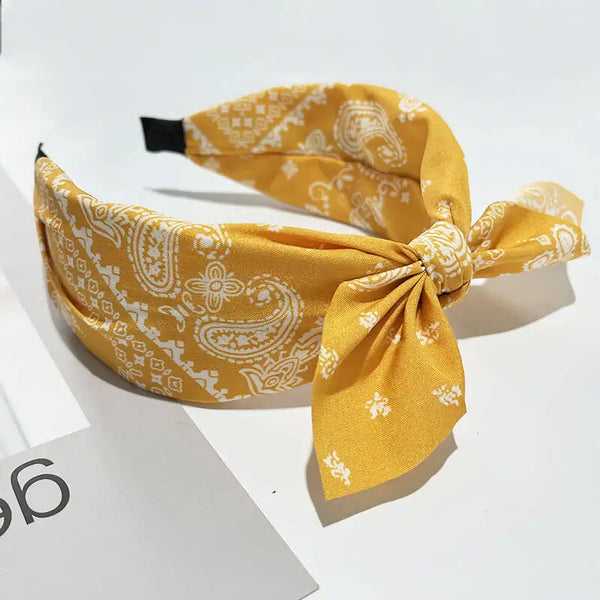 Diadema de seda amarillo mostaza atada en un lazo con un intrincado estampado paisley blanco.