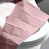 Pink disposable toilet seat covers with water droplets on a white toilet bowl
