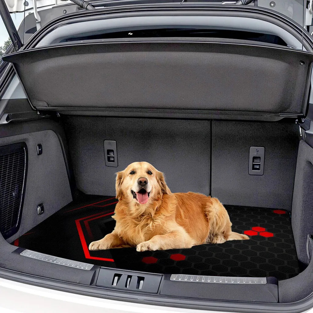 A golden retriever lies on a black and red car trunk mat inside an open vehicle trunk.