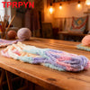 A long, colorful chunky chenille yarn in pink, blue, and purple is displayed on a wooden table.