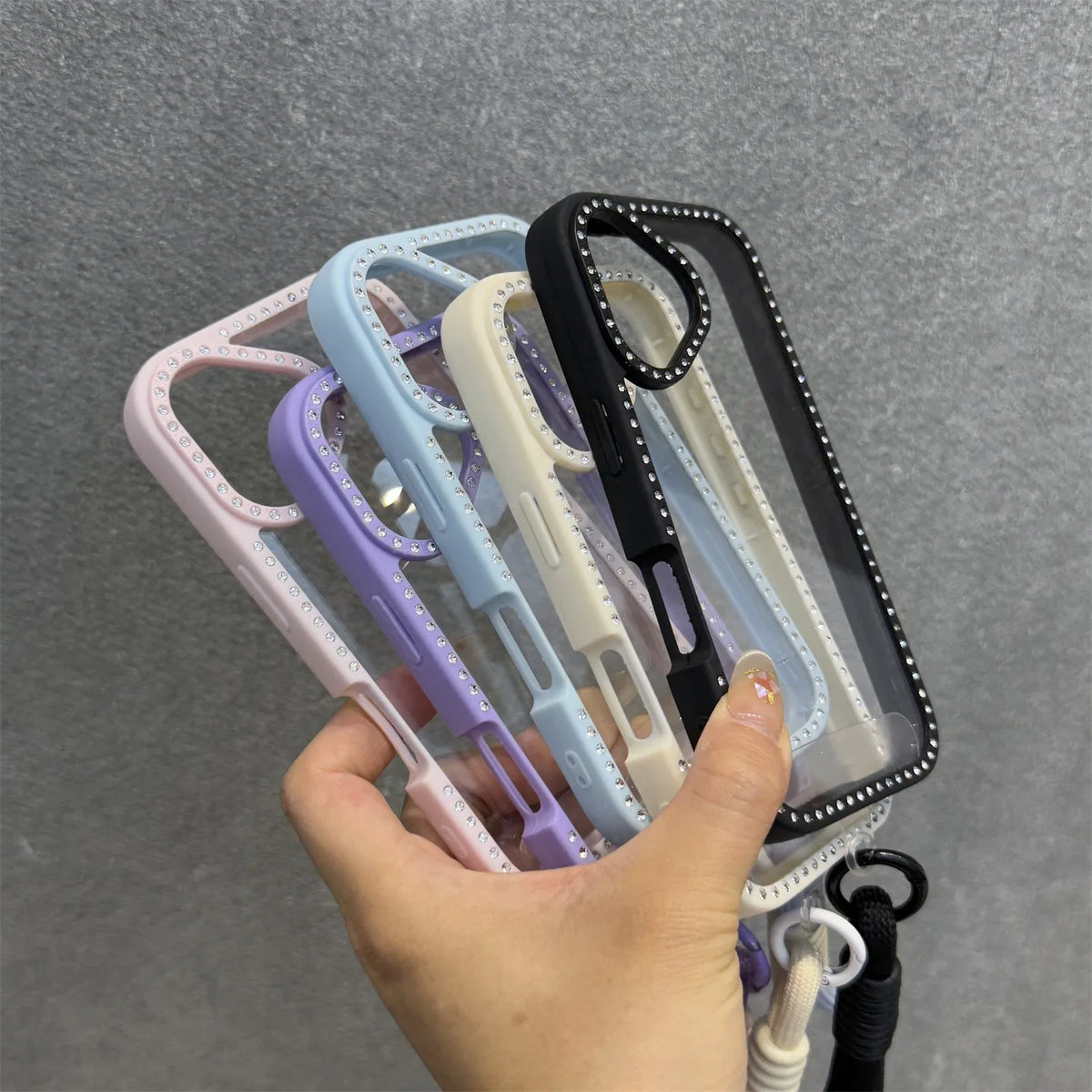 Una mano sostiene una pila de fundas para teléfono transparentes con correas en varios colores pastel.