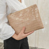A hand holds a beige crocodile-embossed PU leather envelope clutch against a white shirt and black pants.
