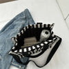 A black and white striped canvas tote bag with inner pockets resting on a white surface next to denim jeans.