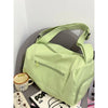 A light green canvas travel tote bag with a strap is shown resting on a gray surface.