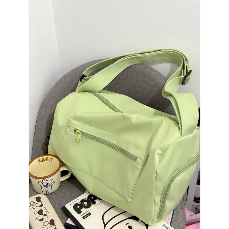 A light green canvas travel tote bag with a strap is shown resting on a gray surface.