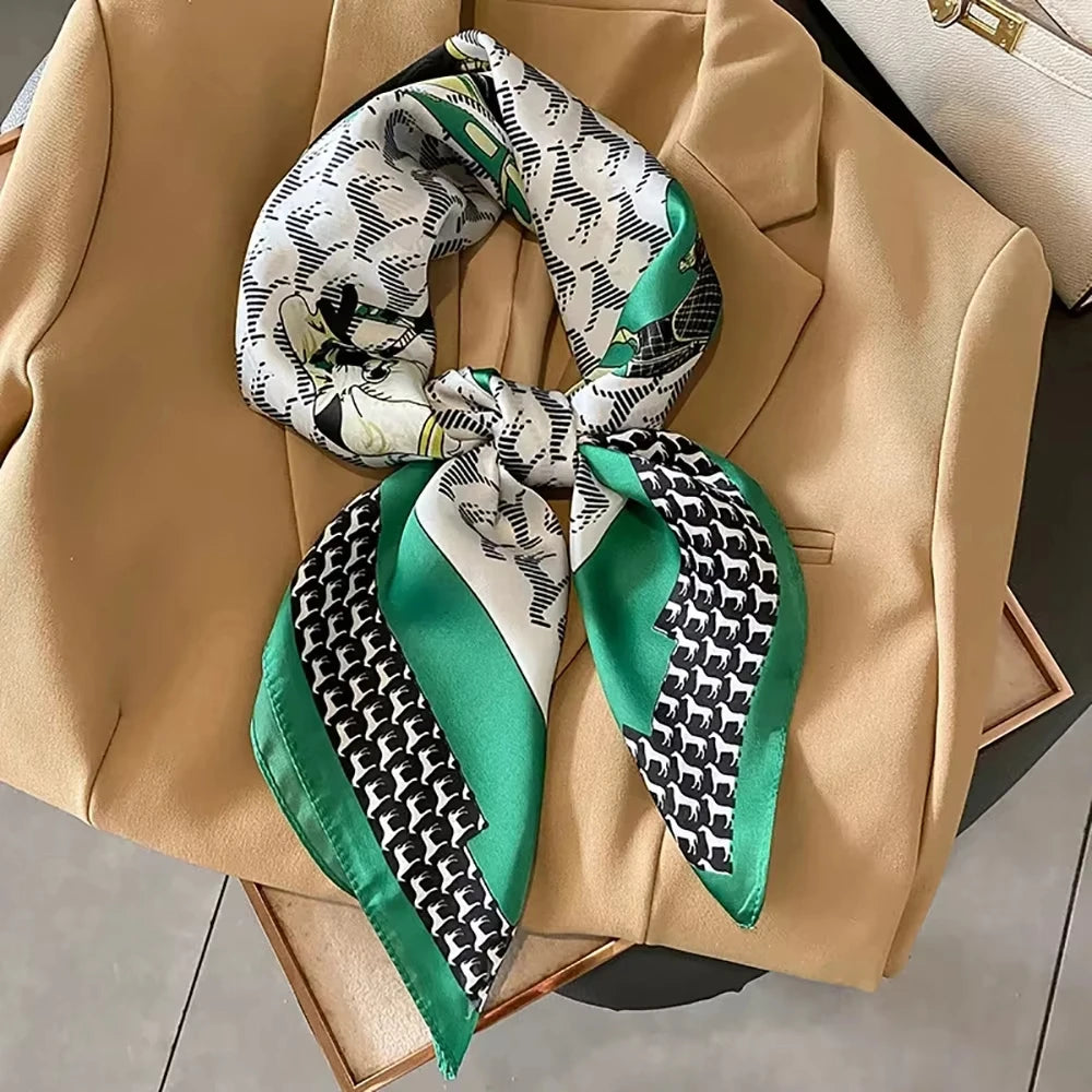 A silk square scarf featuring a black and white geometric pattern with accents of emerald green tied in a knot, displayed on 