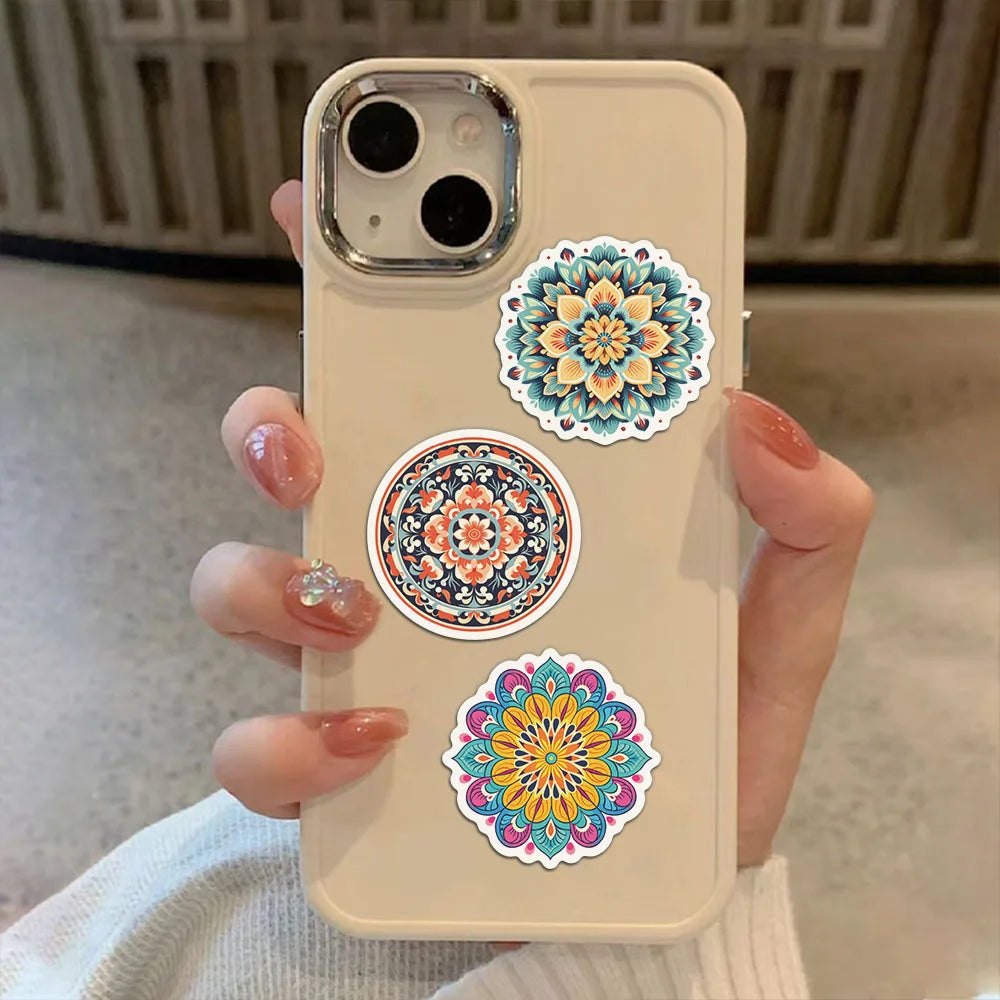 A hand holds a light beige phone case featuring colorful mandala and graffiti stickers.