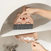 A hand is holding a small, brown cartoon bear broom and dustpan set against a white shelf.