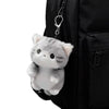 A soft grey cat plush charm hanging from a keychain attached to a black backpack.