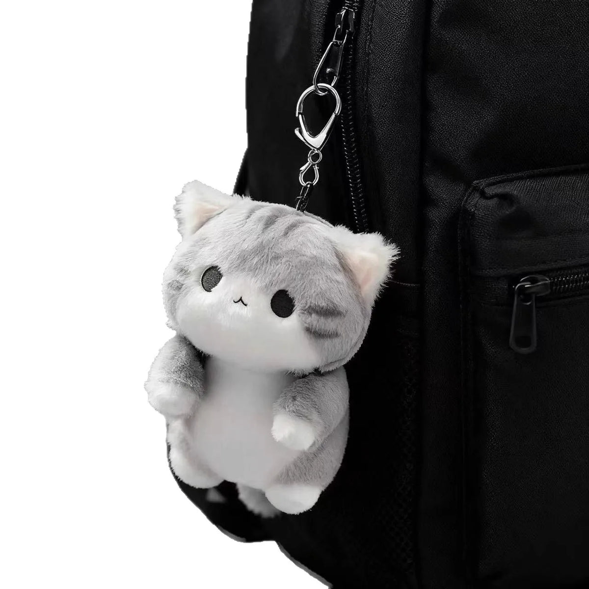 A soft grey cat plush charm hanging from a keychain attached to a black backpack.