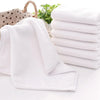 A stack of white soft cotton terry cloth face towels is shown next to a folded towel on a white surface.