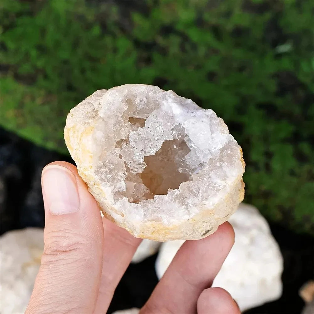 A hand holds a natural agate geode crystal cluster, showing its translucent, pale yellow-white interior.
