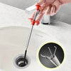 A hand is using a red bendable drain auger with a claw grabber to clear a clog from a white porcelain sink.