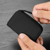 A hand holds a black compact RFID wallet with a zipper on a wooden surface.