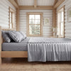 A bedroom featuring a wooden bed with a gray striped satin sheet set and light wood paneling.