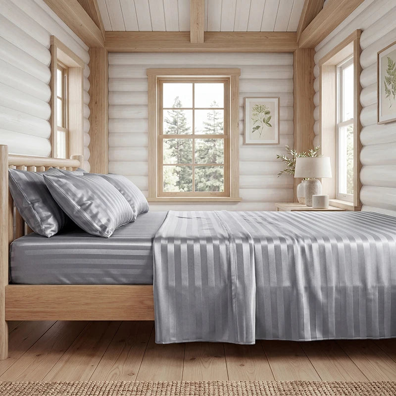 A bedroom featuring a wooden bed with a gray striped satin sheet set and light wood paneling.