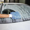 A hand wearing a white glove is using a blue microfiber mitt to wash frost and ice off a car windshield.