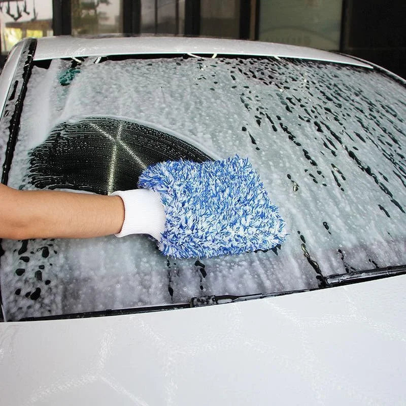 A hand wearing a white glove is using a blue microfiber mitt to wash frost and ice off a car windshield.