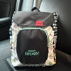 A gray and white backpack featuring a cow print design and a black front pocket, placed on a dark car seat.