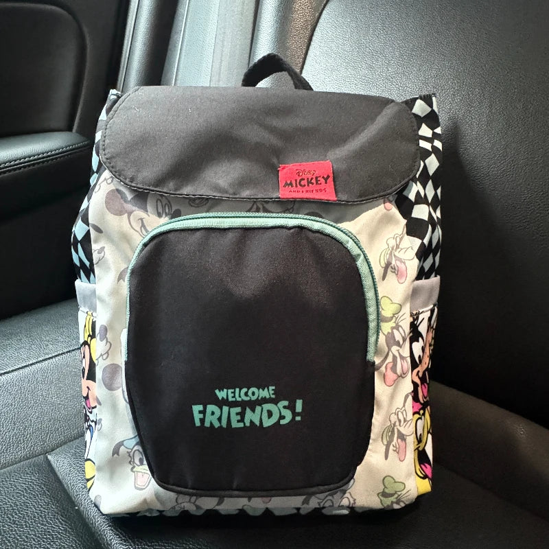 A gray and white backpack featuring a cow print design and a black front pocket, placed on a dark car seat.