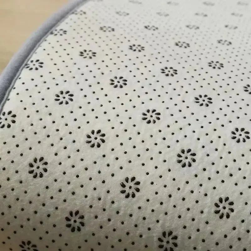 Close-up view of a white plush silk-touch area rug with small black floral and dot patterns.
