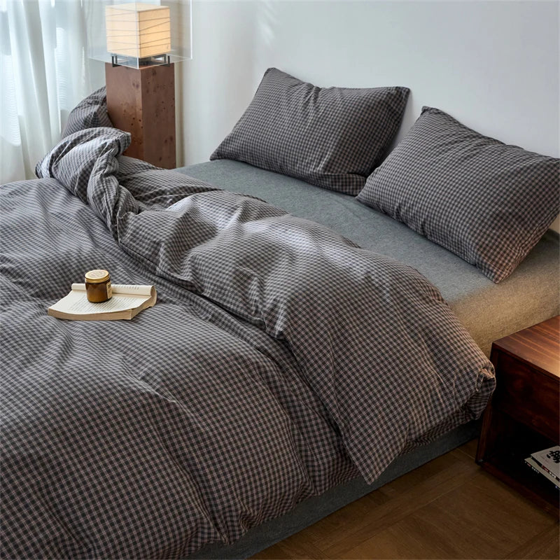 A plaid duvet cover in gray and white tones is displayed on a bed with sheer curtains and a wooden lamp.