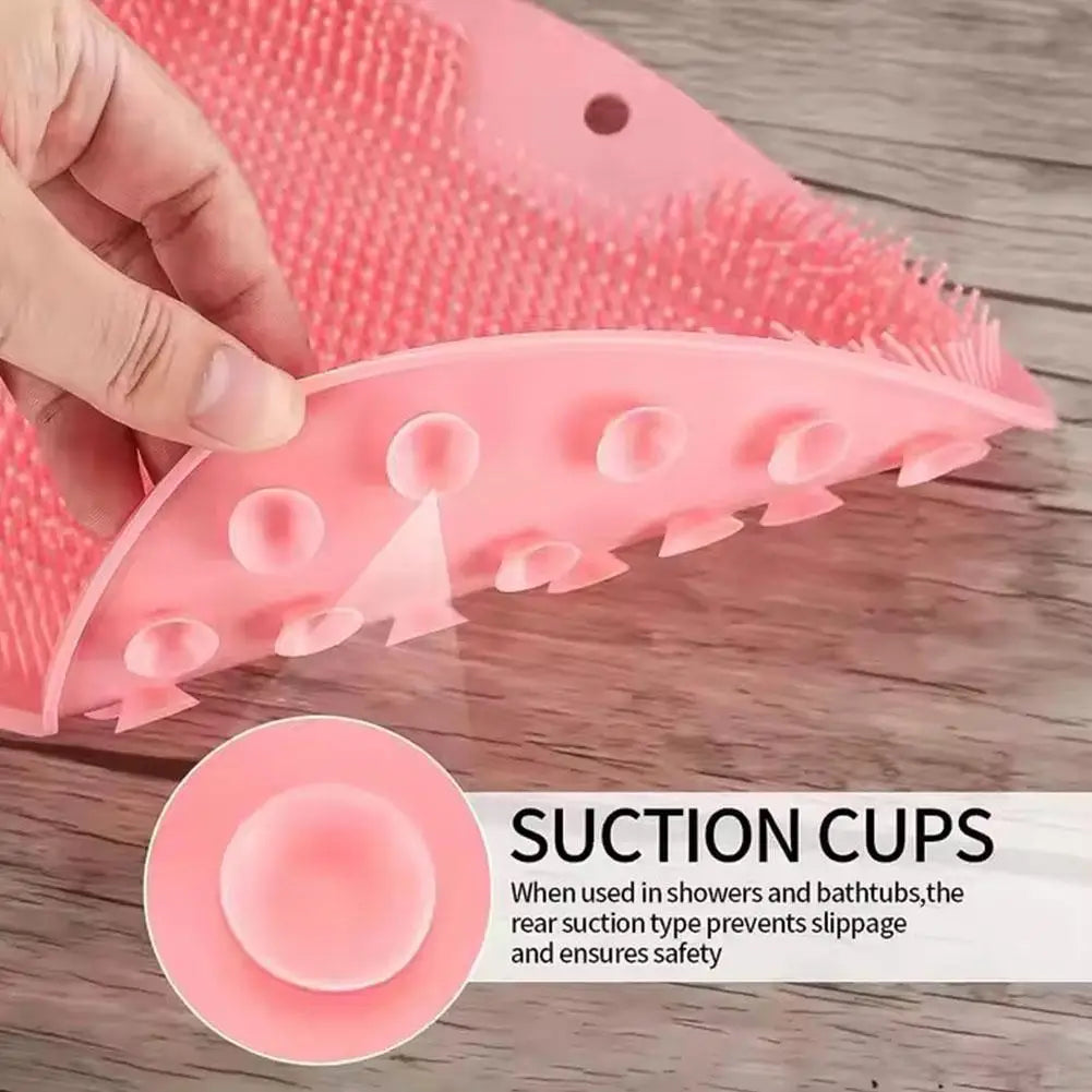 A hand is holding a pink silicone foot scrubber with suction cups, designed for use in showers and bathtubs.