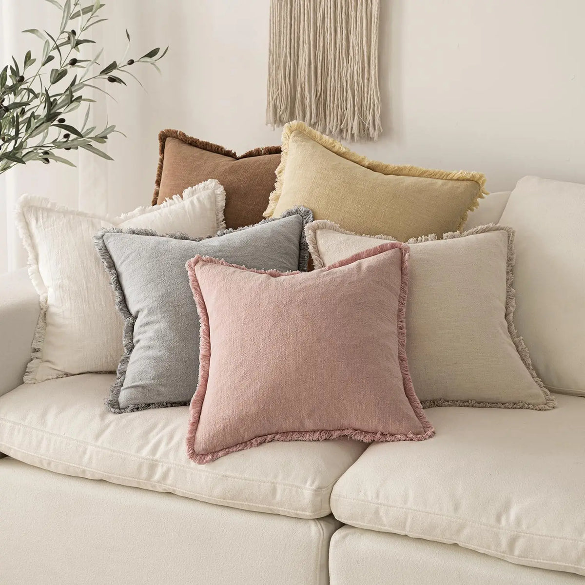 A collection of boho fringe throw pillows in natural linen textures and muted earth tones on a light sofa.