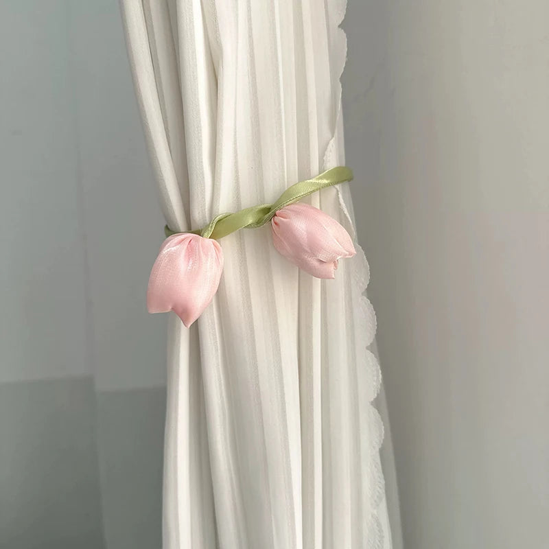 Pink tulip fabric tie backs with green ribbon attached to a white pleated curtain.