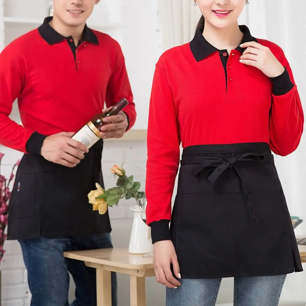 A woman wearing a red long-sleeved shirt and a black half apron with pockets standing next to a man.