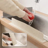 A hand is rinsing a tomato under a flexible silicone sink splash guard in a kitchen sink.