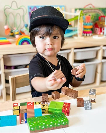 A toddler wearing a black hat is playing with colorful magnetic building blocks on a wooden table.