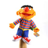An Elmo hand puppet, a soft orange plush toy with black hair and a wide smile, wearing a striped shirt and blue pants.