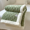 A green and white double-layer fleece throw blanket folded on a white bed.