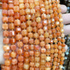 A hand holds a strand of square faceted natural orange and yellow amber beads for jewelry making.