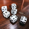 A set of white and black Gothic skull dice scattered on a dark wooden surface.