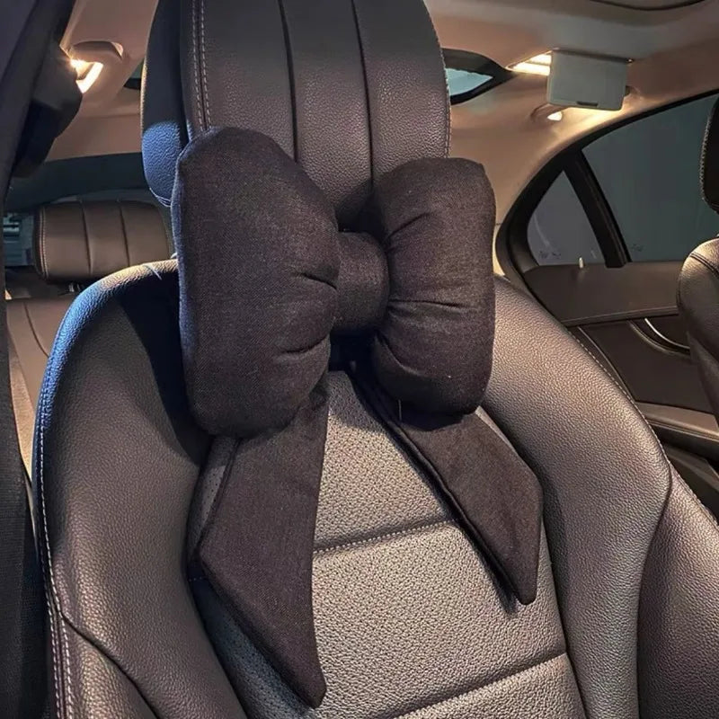 A black butterfly bow tie neck pillow with a dark fabric cover is shown inside a car seat.