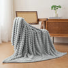 A soft gray brushed flannel throw blanket draped on a wooden surface next to a desk.