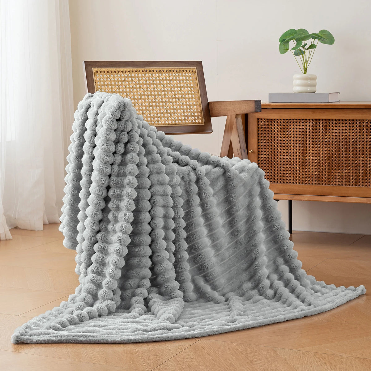 A soft gray brushed flannel throw blanket draped on a wooden surface next to a desk.