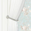 Silver U-shaped tieback hooks used to hold white curtains against a floral patterned fabric.
