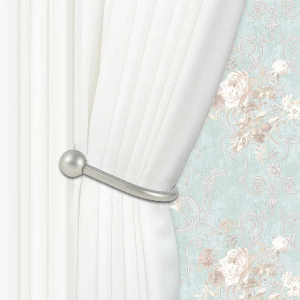 Silver U-shaped tieback hooks used to hold white curtains against a floral patterned fabric.