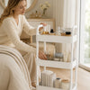 A woman is using a white 3-tier rolling utility cart with wheels for storage in a bright room.