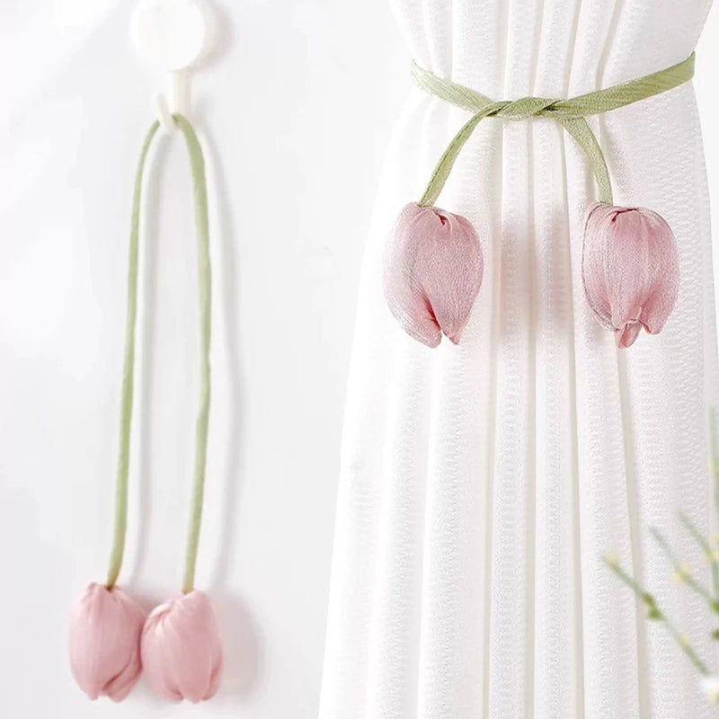 A set of pink tulip fabric tie backs used to secure a white curtain.