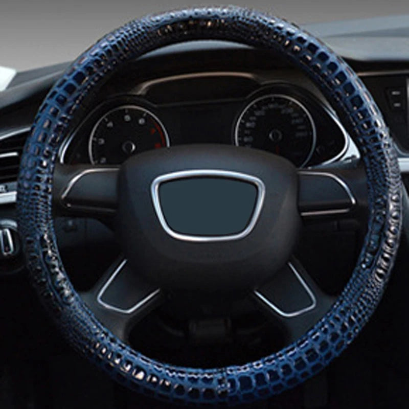 A close-up view of a black car steering wheel with a blue crocodile grain leather cover.
