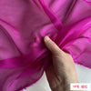 A hand is holding and draping bright magenta silk chiffon fabric.