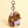 A brown capybara plush toy with a purple ear and a striped purple accessory attached to a metal keychain.