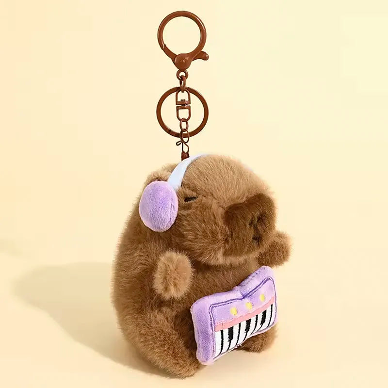 A brown capybara plush toy with a purple ear and a striped purple accessory attached to a metal keychain.