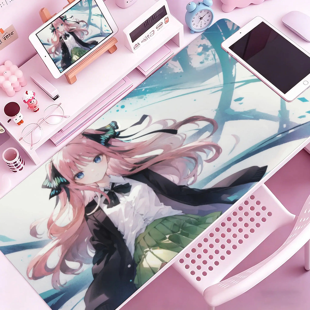 A pink anime girl illustration on a mouse pad featuring pink hair and dark clothing, placed on a desk with electronic devices